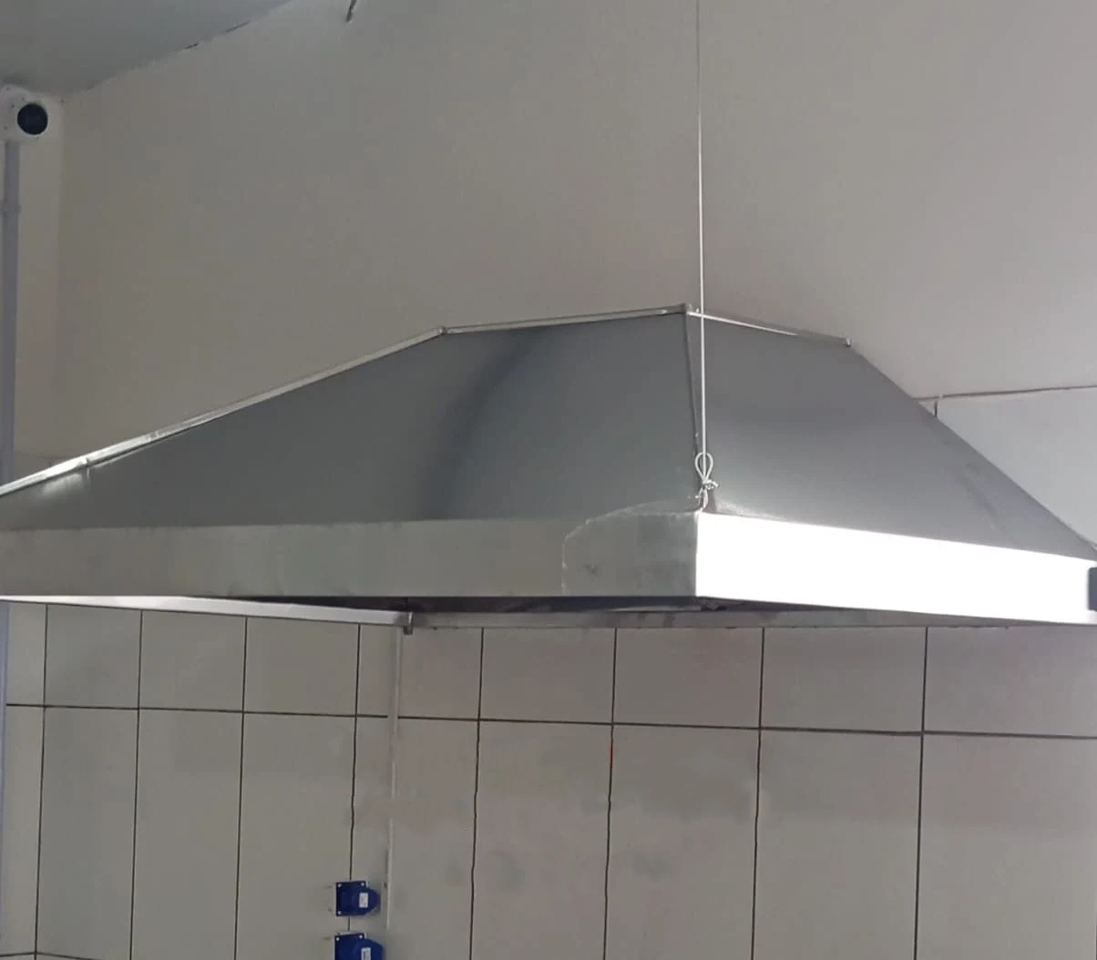 Coifa de aço inox sobre área de cozinha com parede revestida de azulejos